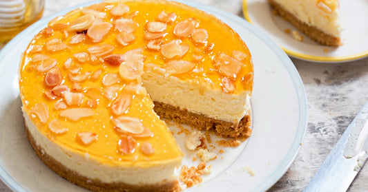 A Greek-style yogurt cheesecake with a brown crust featuring a thick golden honey topping containing almond shavings.