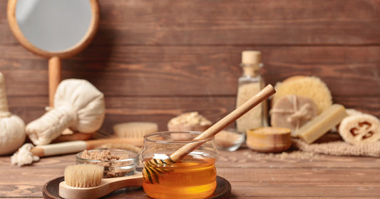 A glass jar of honey with a honey dipper inside of it sits on a table with brushes, sponges, and other spa essentials.