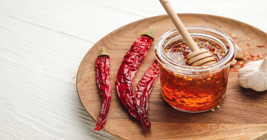 Three dried red chili peppers and a head of garlic sit next to a jar of honey with chili flakes floating in it.