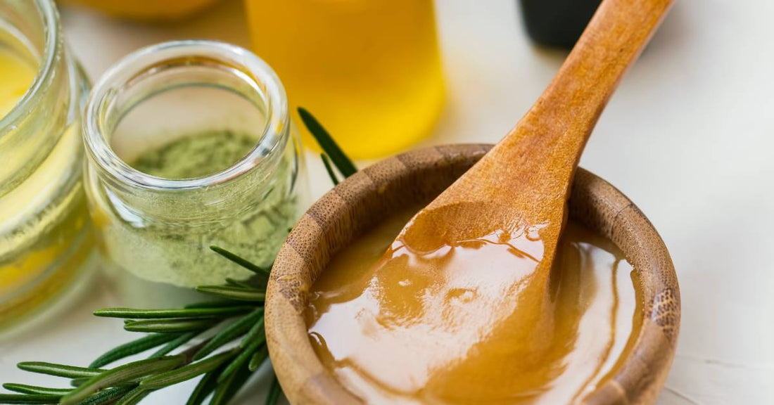 A wooden spoon sticks out of a small wooden bowl with a honey mixture inside it on a table with other ingredients.