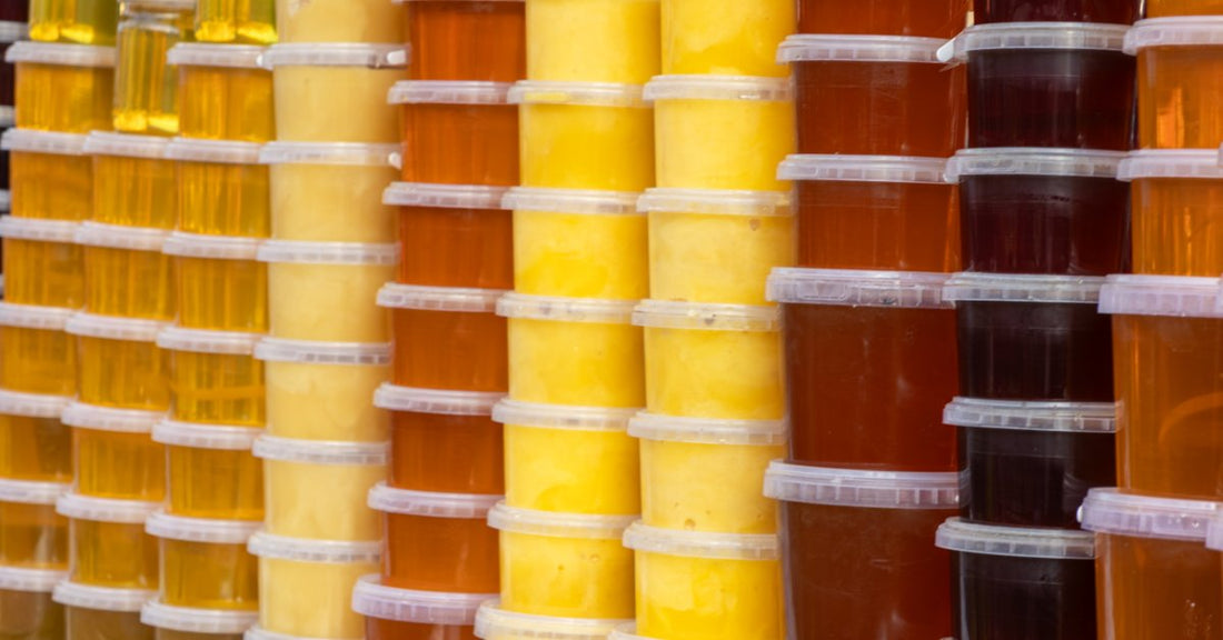 Rows of clear plastic tubs display honey in shades ranging from pale yellow and golden amber to deep brown.