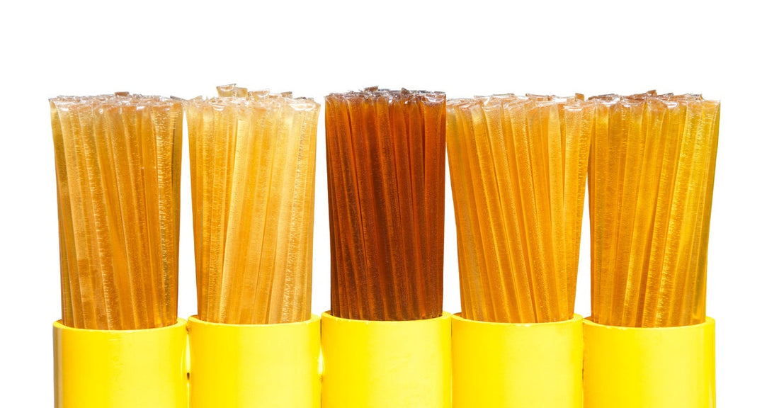 Rows of golden and amber adhesive sticks are grouped upright in yellow sleeves against a plain white background.
