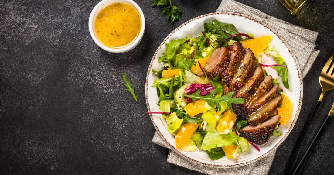 A delicious-looking plate of sliced duck accompanied by green salad and a honey mustard dressing on the side.