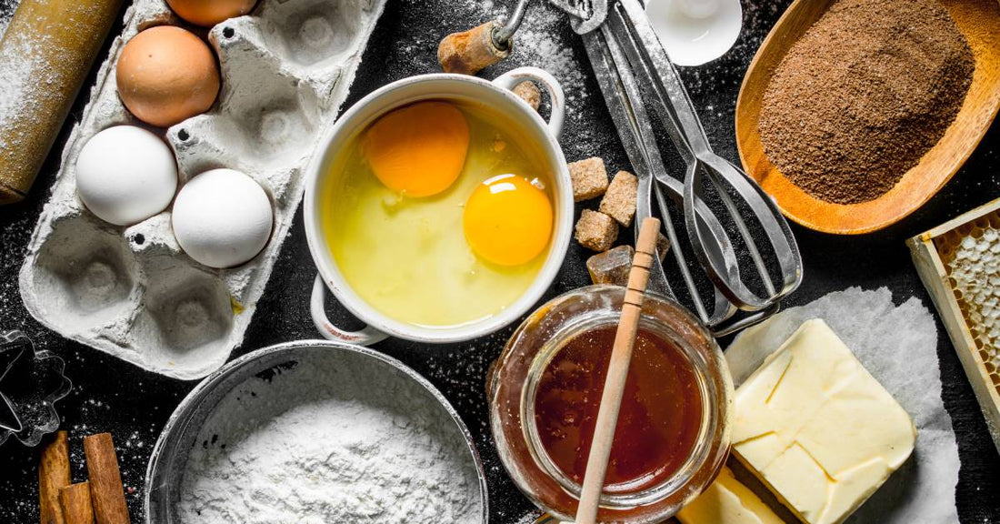 A collection of baking ingredients seen from above, including honey, eggs, flour, cinnamon, and butter