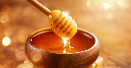 A honey dipper, up close. A person takes the dipper out of a bowl of honey while honey slowly drips off of it.